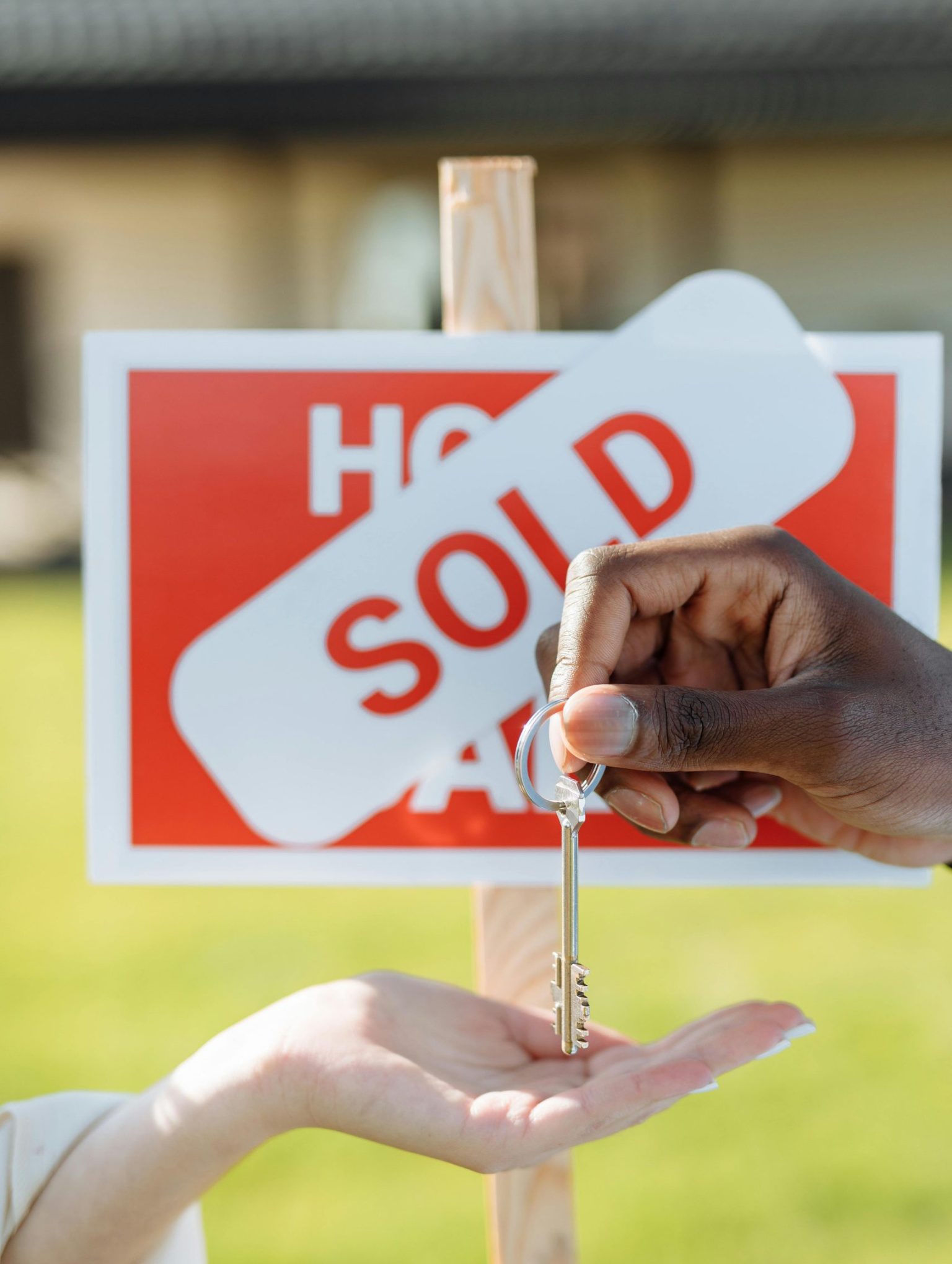 Key exchange in front of a sold sign, symbolizing successful real estate transaction.