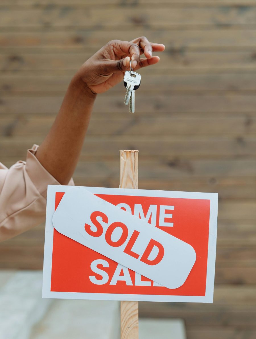 A hand holding keys above a sold sign in a real estate environment, symbolizing a completed property sale.